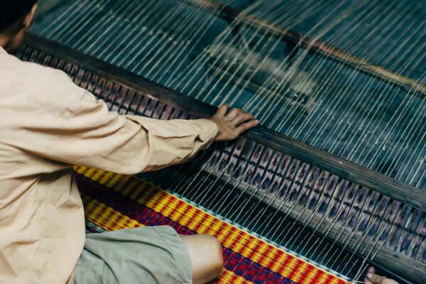 A person is weaving on a loom with a basket